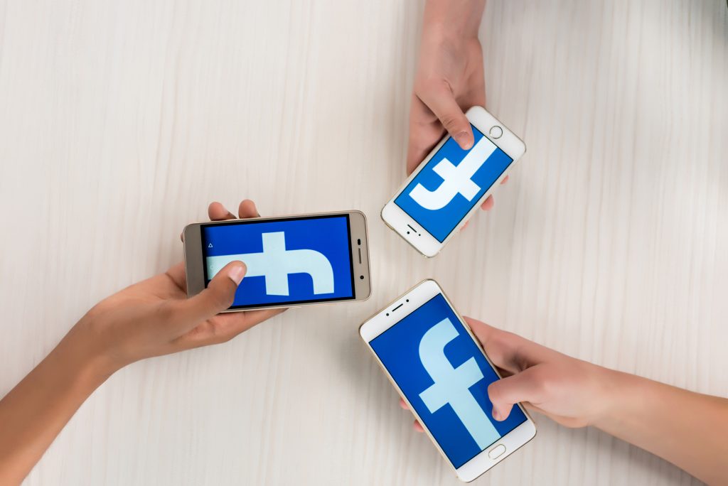 hands holding cell phones with Facebook logo